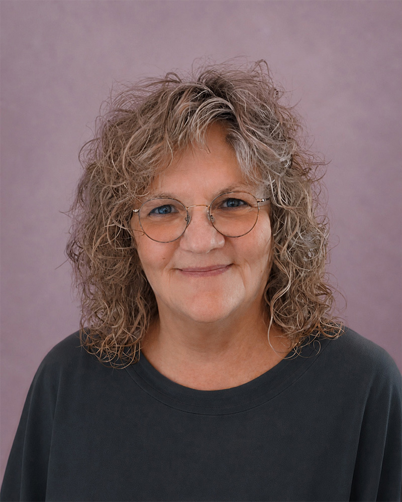 Porträtfoto von Susanne Dehring, Gestalt- und Traumatherapeutin. Sie blickt lächelnd in die Kamera und trägt eine runde Brille vor einem fliederfarbenen Hintergrund.